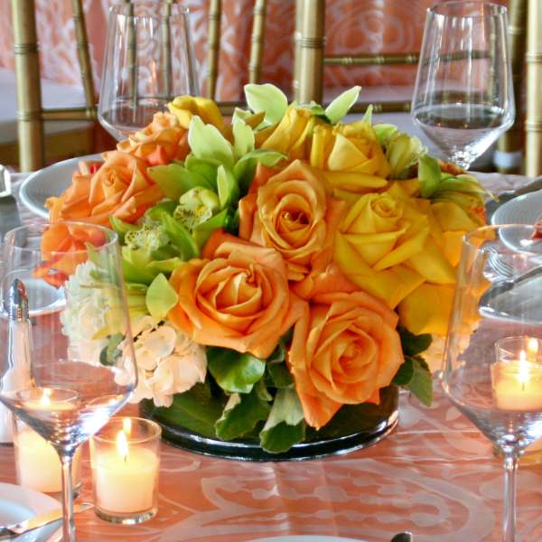 Orange and yellow rose centerpiece on a table with candles and wine glasses
