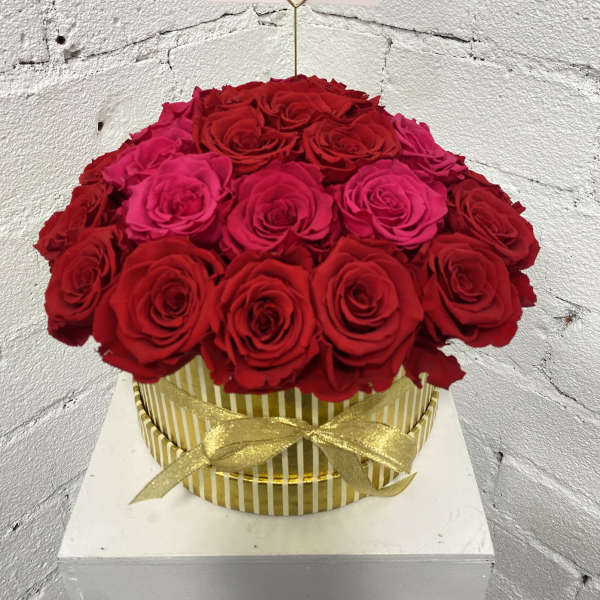 Round box of red and pink roses with a gold ribbon and card holder