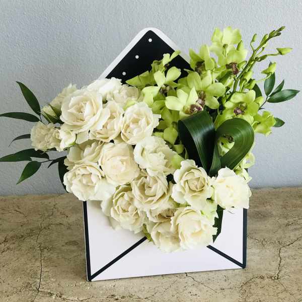 White roses and green orchids arranged in a white envelope box
