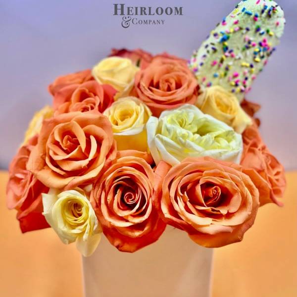 Orange and cream roses in a white square vase with a sprinkle-covered treat