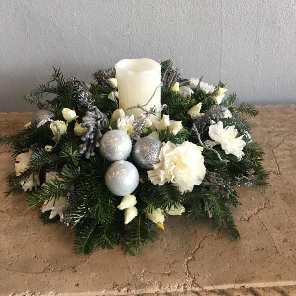 Holiday centerpiece with a white pillar candle, white flowers, and silver ornaments