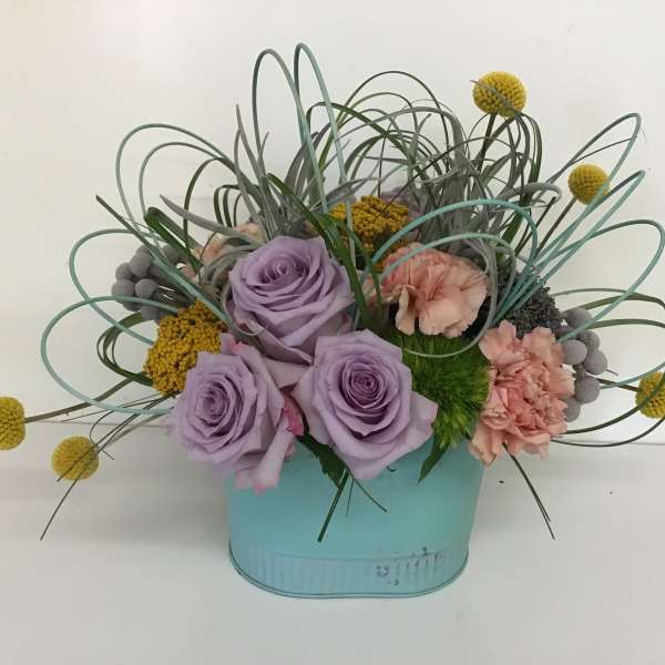 Lavender roses and pink carnations in a blue container with looping grass