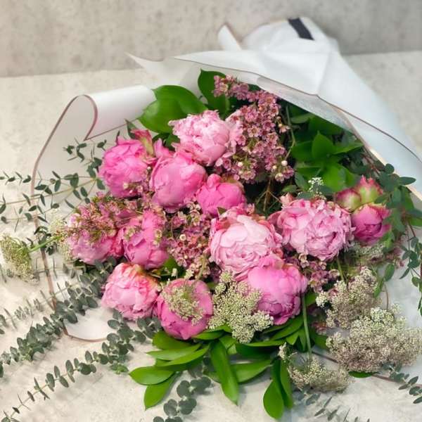 Pink peony bouquet wrapped in white paper with greenery