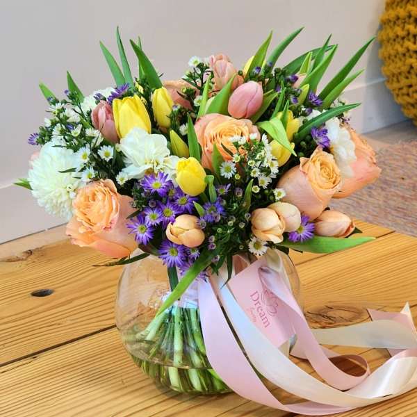 Mixed bouquet of tulips, roses, and daisies in a round glass vase