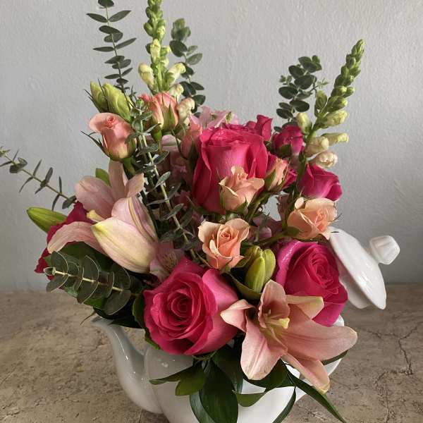 Pink roses and lilies arranged in a white ceramic teapot.