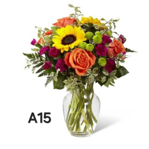 Mixed bouquet of orange roses, yellow sunflower, and magenta flowers in a glass vase