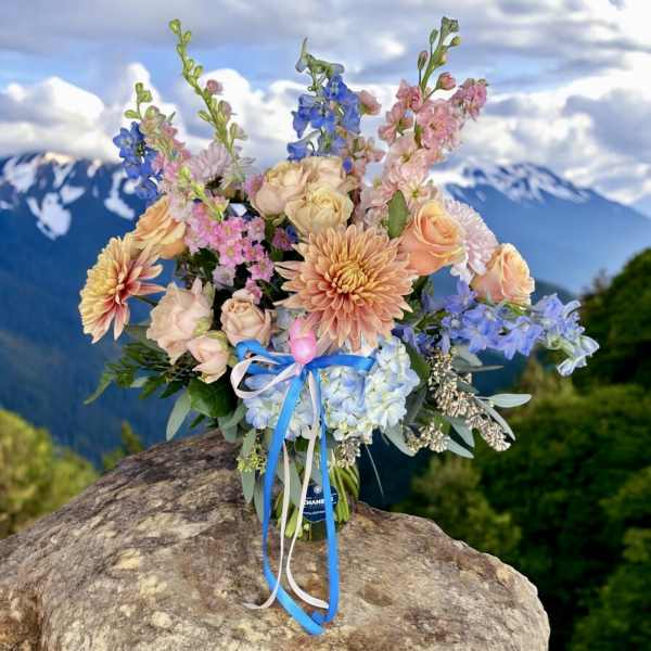 Mixed bouquet of pastel flowers in a glass vase with blue ribbon