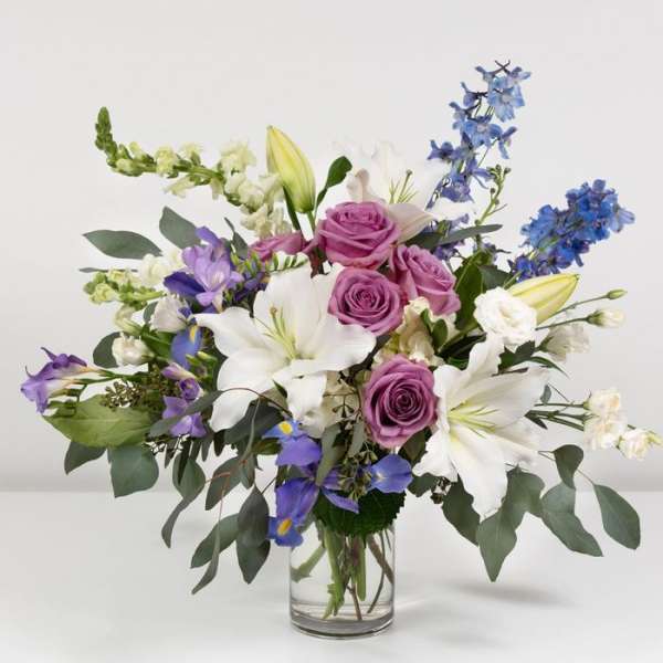 Bouquet of purple roses, white lilies, and blue flowers in a glass vase