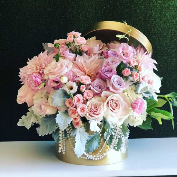 Pink and white roses arranged in a gold hatbox with pearl strands