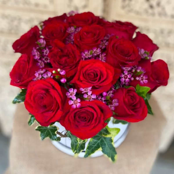 Bouquet of red roses with small purple filler flowers in a white vase