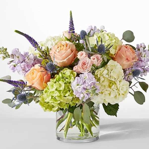 Mixed bouquet of peach roses, hydrangeas, and purple flowers in a glass vase