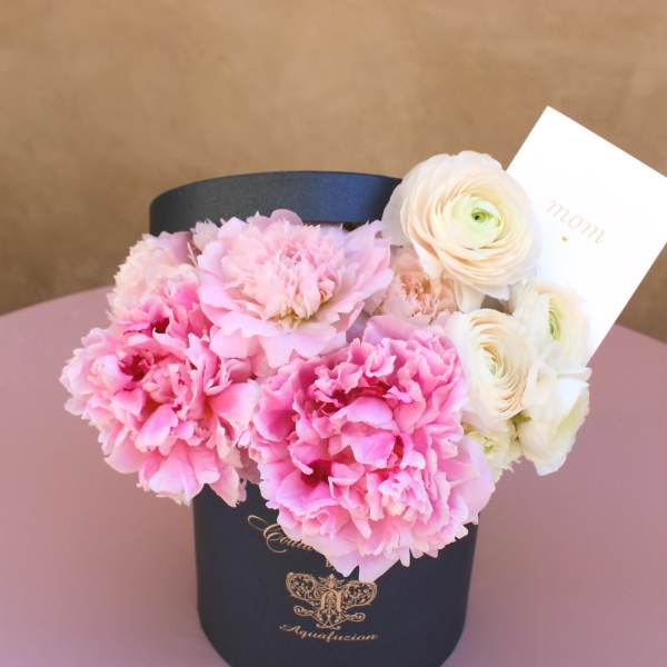 Pink carnations and white ranunculus in a black hat box