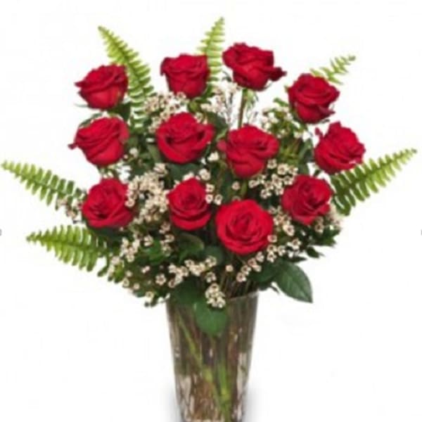 Red roses arranged in a clear glass vase with fern accents