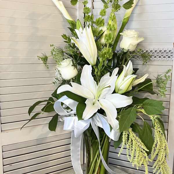 White lilies and roses in a clear glass vase with a white ribbon