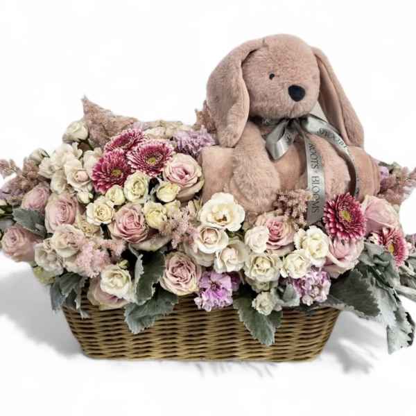 Basket of pastel flowers with a plush bunny