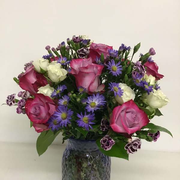 Pink and white roses with purple daisies in a glass vase