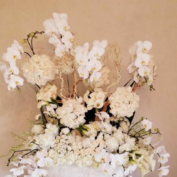 Large white floral arrangement in a white vase with orchids and roses