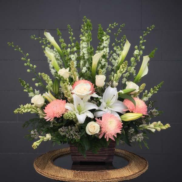 Large floral arrangement with white lilies, roses, and pink mums in a wooden container