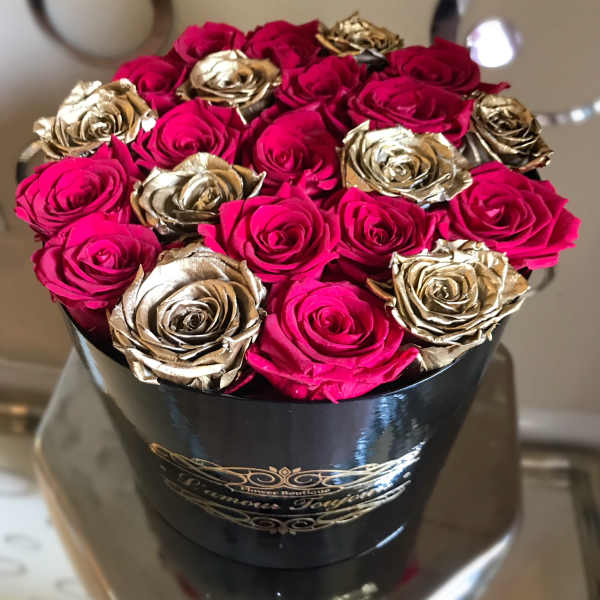 Pink and gold roses arranged in a black hat box
