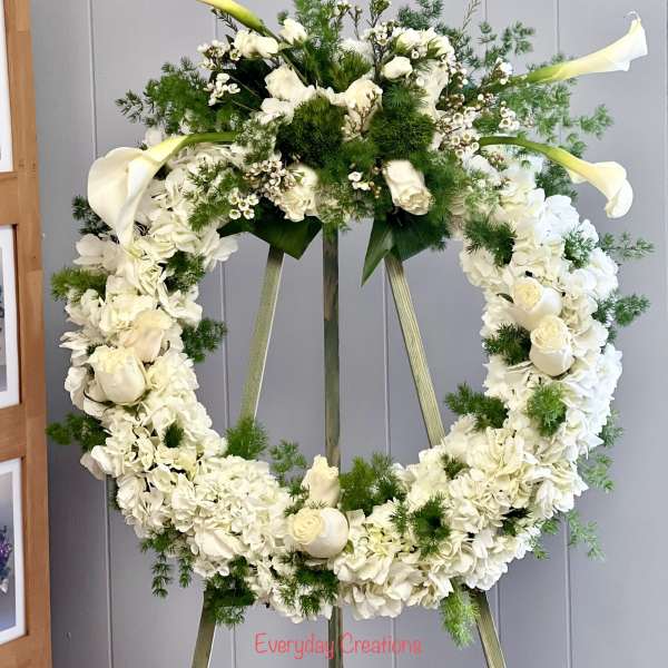 White floral wreath on an easel with calla lilies and roses