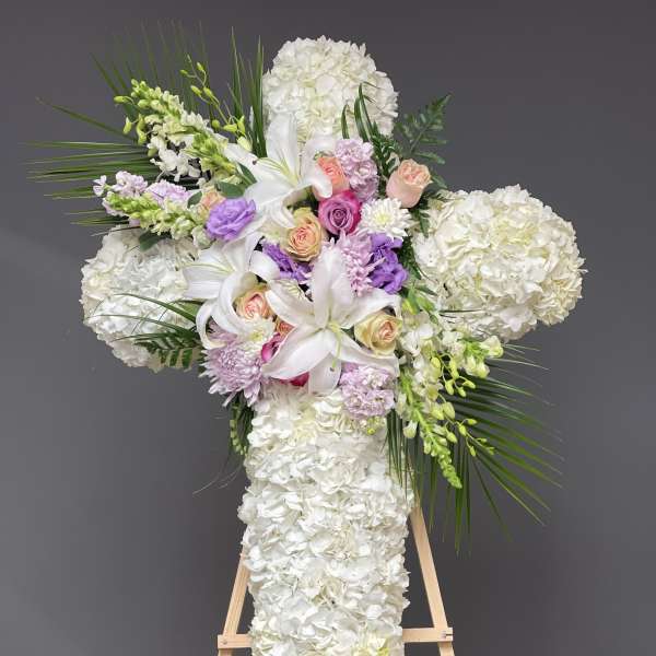 White floral cross arrangement with lilies, roses, and hydrangeas on an easel