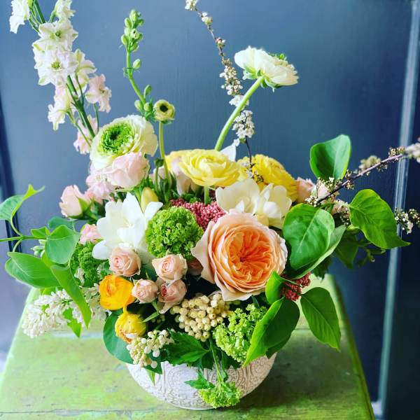 Mixed bouquet in a patterned bowl vase with peach, yellow, white, and green blooms