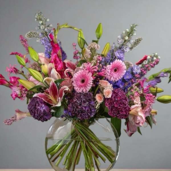 Mixed bouquet of pink, purple, and white flowers in a clear glass vase
