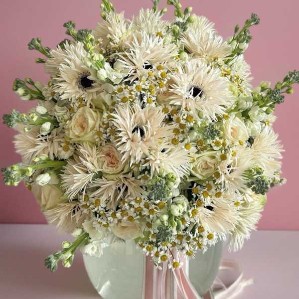 Creamy white bouquet with roses and daisy-like flowers in a pale vase