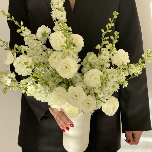 White floral arrangement in a white pedestal vase held against a black outfit