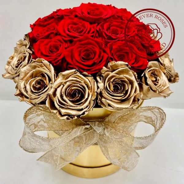 Red and gold roses arranged in a round gold box with a sheer ribbon bow.