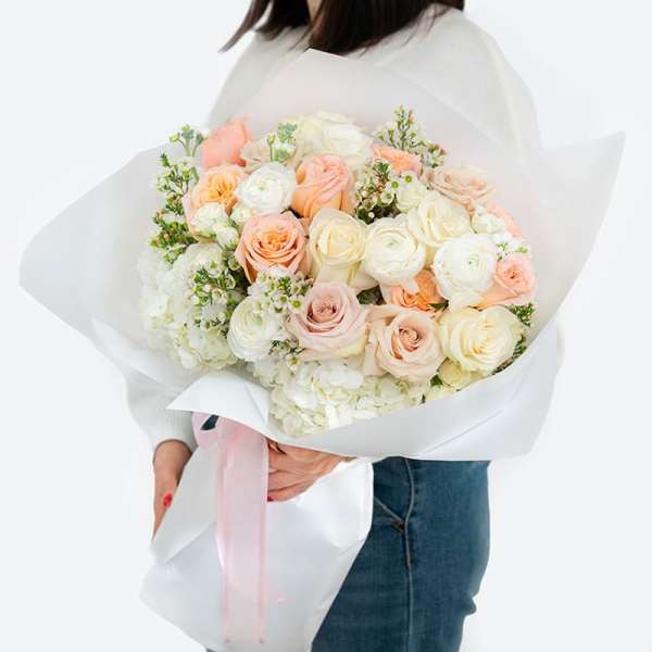 Large bouquet of blush, peach, and white roses wrapped in white paper