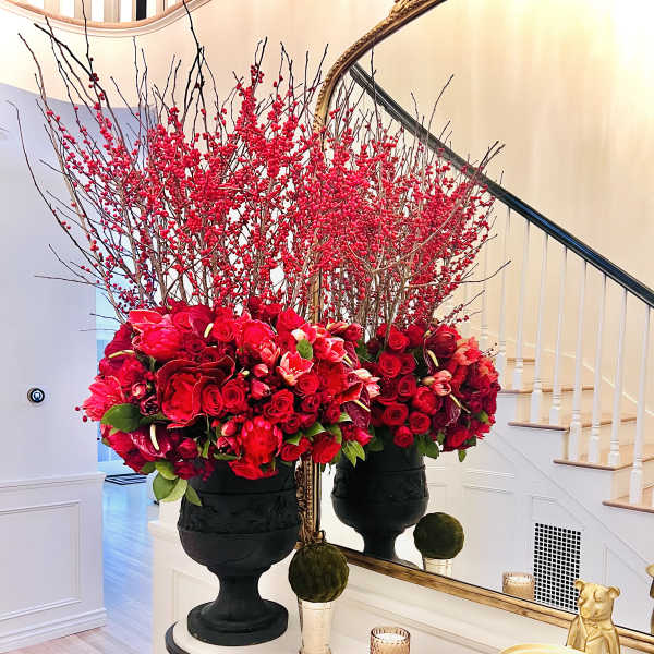 Two large red floral arrangements in black urns on a console table