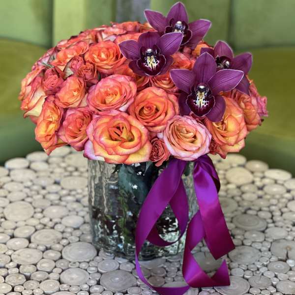 Bouquet of orange-pink roses and purple orchids in a glass vase