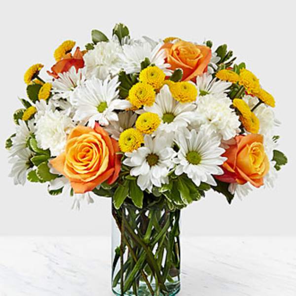 Mixed bouquet of orange roses, white daisies, and yellow poms in a clear glass cylinder vase