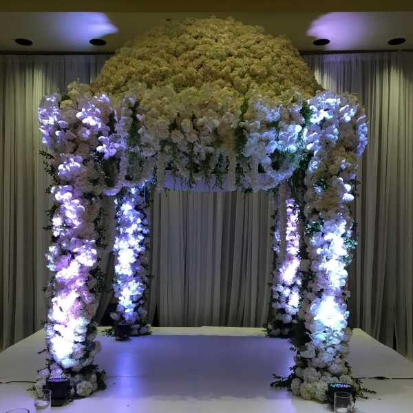 Large white floral wedding arch on a stage with purple lighting