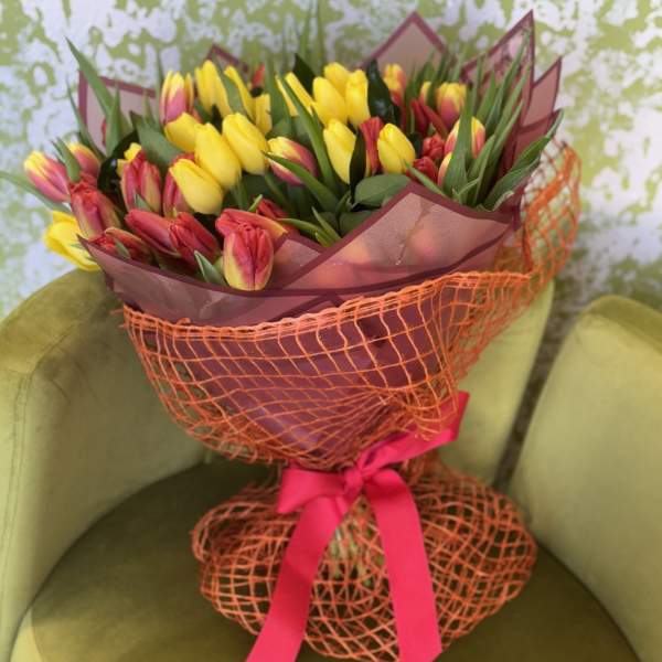 Bouquet of yellow and red tulips wrapped in orange mesh with a pink ribbon