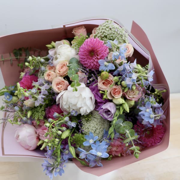 Mixed bouquet of pink, purple, blue, and white flowers wrapped in pink paper