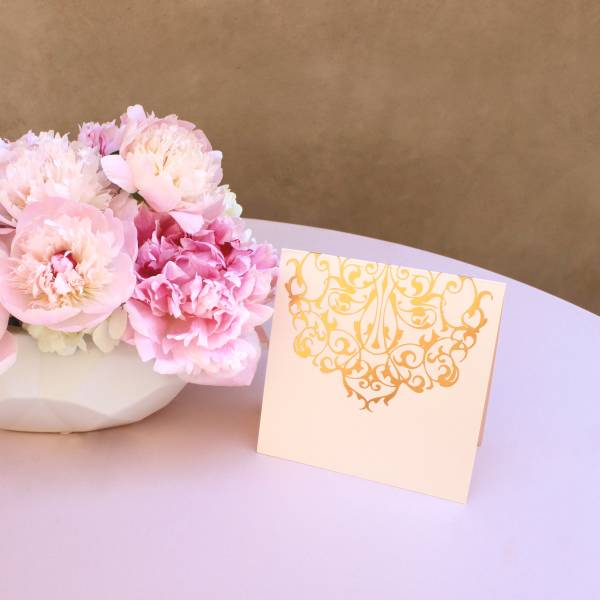 Pink peonies in a white bowl with a decorative card beside them
