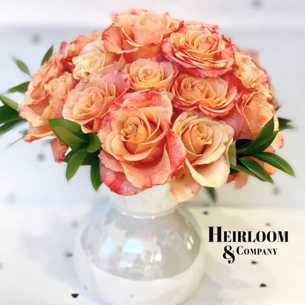 Peach and coral roses arranged in a clear glass vase