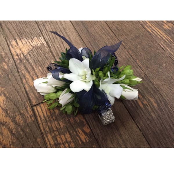 White floral corsage with dark blue ribbon accents on a wooden surface