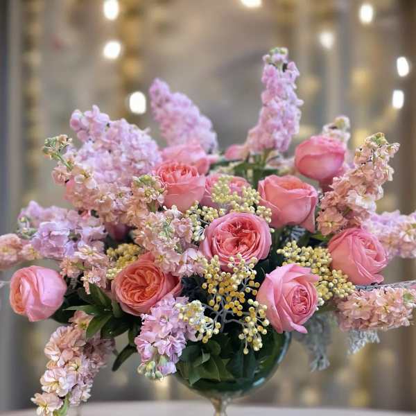 Pink roses and lilac flowers arranged in a glass compote vase