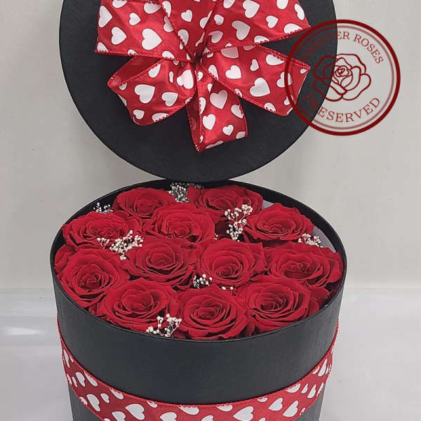 Red roses in a round black gift box with a heart-patterned ribbon bow
