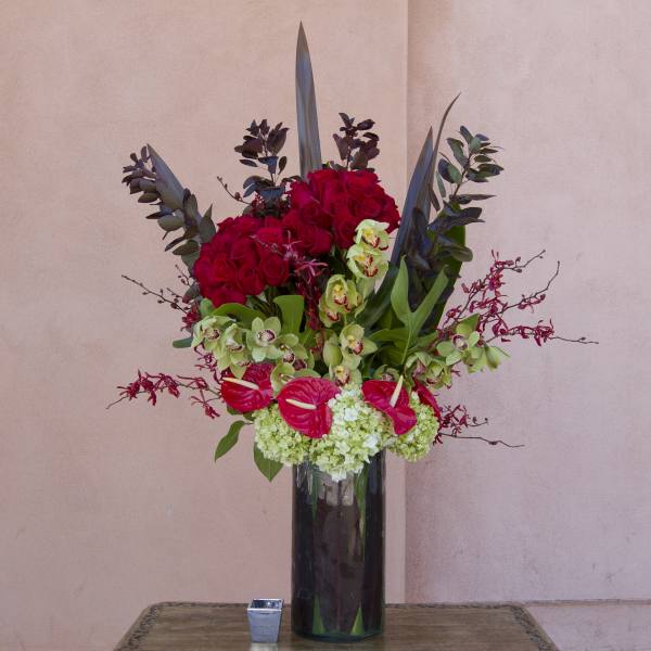 Tall arrangement of red roses, green orchids, and anthuriums in a dark vase