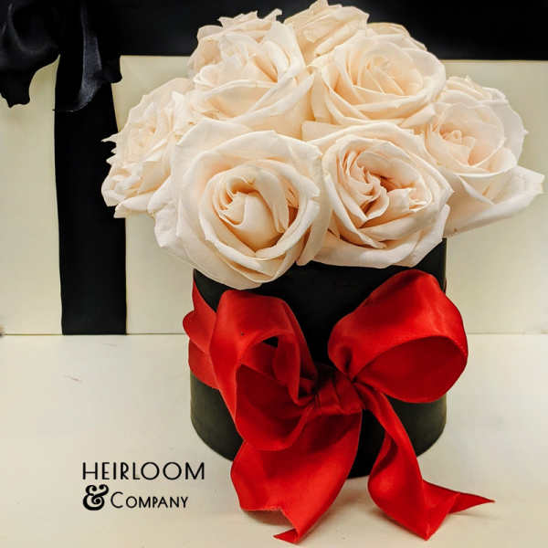 Cream roses in a black hatbox with a red ribbon