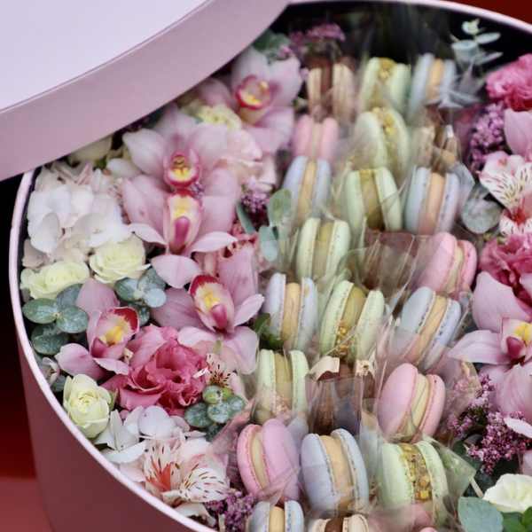 Round pink gift box filled with flowers and pastel macarons