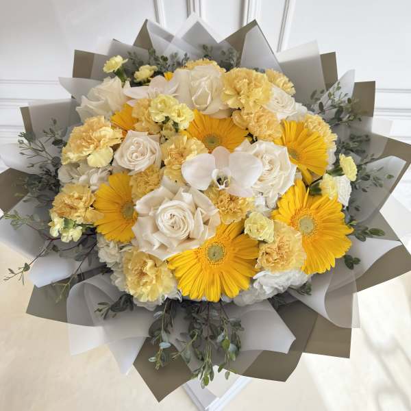 Bouquet of yellow gerbera daisies, white roses, and pale carnations wrapped in paper