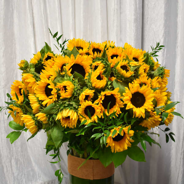 Large arrangement of yellow sunflowers in a tall clear glass vase on a table