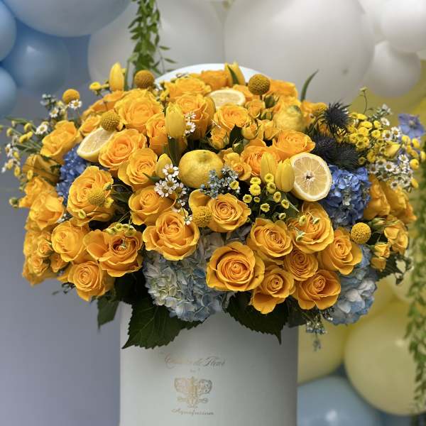 Yellow rose arrangement in a white hat box with blue hydrangeas and lemon slices