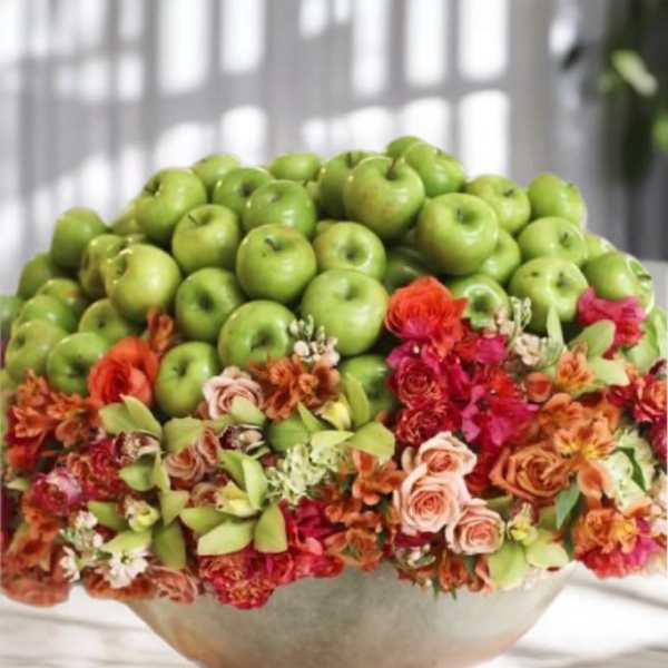 Bowl arrangement topped with green apples and colorful flowers