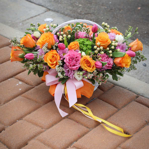Basket arrangement of orange and pink roses with ribbon